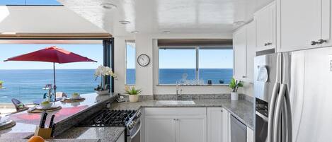Een moderne keuken met uitzicht op de oceaan, voorzien van een roestvrijstalen koelkast, granieten aanrecht en witte kastjes.