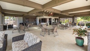 A spacious outdoor patio with multiple seating areas, including wicker sofas and round tables, and a central bar area.