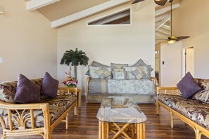 A spacious living room with a high ceiling, a large sofa set, a glass coffee table, and a decorative plant.
