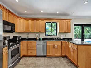 A modern kitchen with wooden cabinets, stainless steel appliances, and a large window overlooking greenery. - Vidal Manor | Walk to Wilton Drive + Heated Pool (Wilton Manors)
