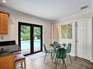A dining area with a pool view, a kitchen with a grill, and a door leading outside. - Vidal Manor | Walk to Wilton Drive + Heated Pool (Wilton Manors)