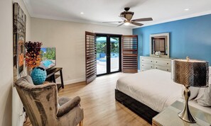 Quarto com cama, escrivaninha, cadeira, ventoinha no teto e vista para o exterior.