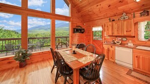 A wooden cabin with a dining area, kitchen, and large windows offering a mountain view. - Bearfoot Memories: 180 Degree Views, Hot Tub (Gatlinburg)