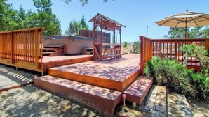 Una terraza de madera con un jacuzzi, un espacio de estar cubierto y una pérgola.
