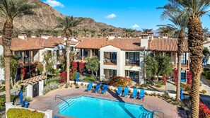A resort with a swimming pool, palm trees, and buildings with red-tiled roofs.