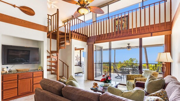 Ein großzügiger Wohnbereich mit einer großen Couch, einem Fernseher, einer Holztreppe und einem Balkon mit Gartenmöbeln.