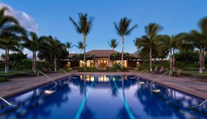 A pool area with a house in the background, surrounded by palm trees.