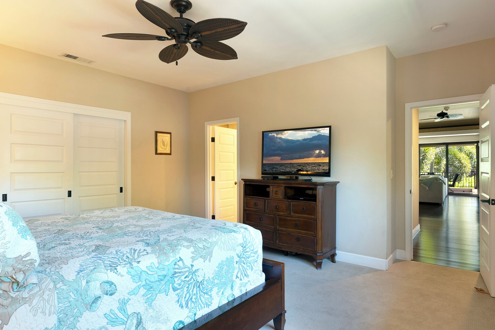 A bedroom with a bed, dresser, television, and a ceiling fan.