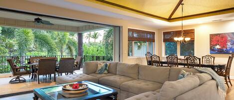 A spacious living area with a large sectional sofa, a glass coffee table, and a dining area with a wooden table and chairs.