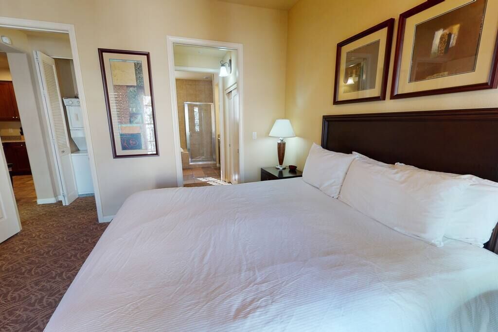 Una habitación de hotel con una cama grande, una mesita de noche, una lámpara y una puerta que da a un baño.