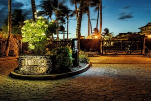 A stone pathway leading to a well-lit sign with the name 'Kali Kai' surrounded by lush greenery and palm trees.