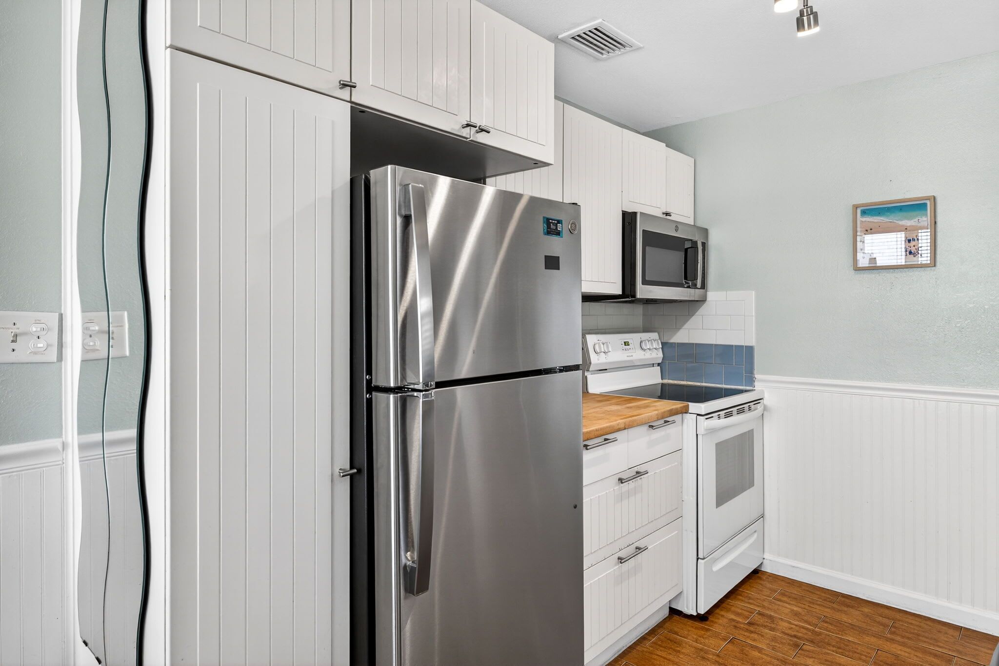 A kitchen with white cabinets, stainless steel appliances, a microwave, and wooden flooring.