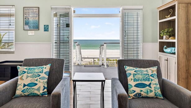 Una habitación con dos sillones, una mesita y vista a la playa a través de puertas abiertas.