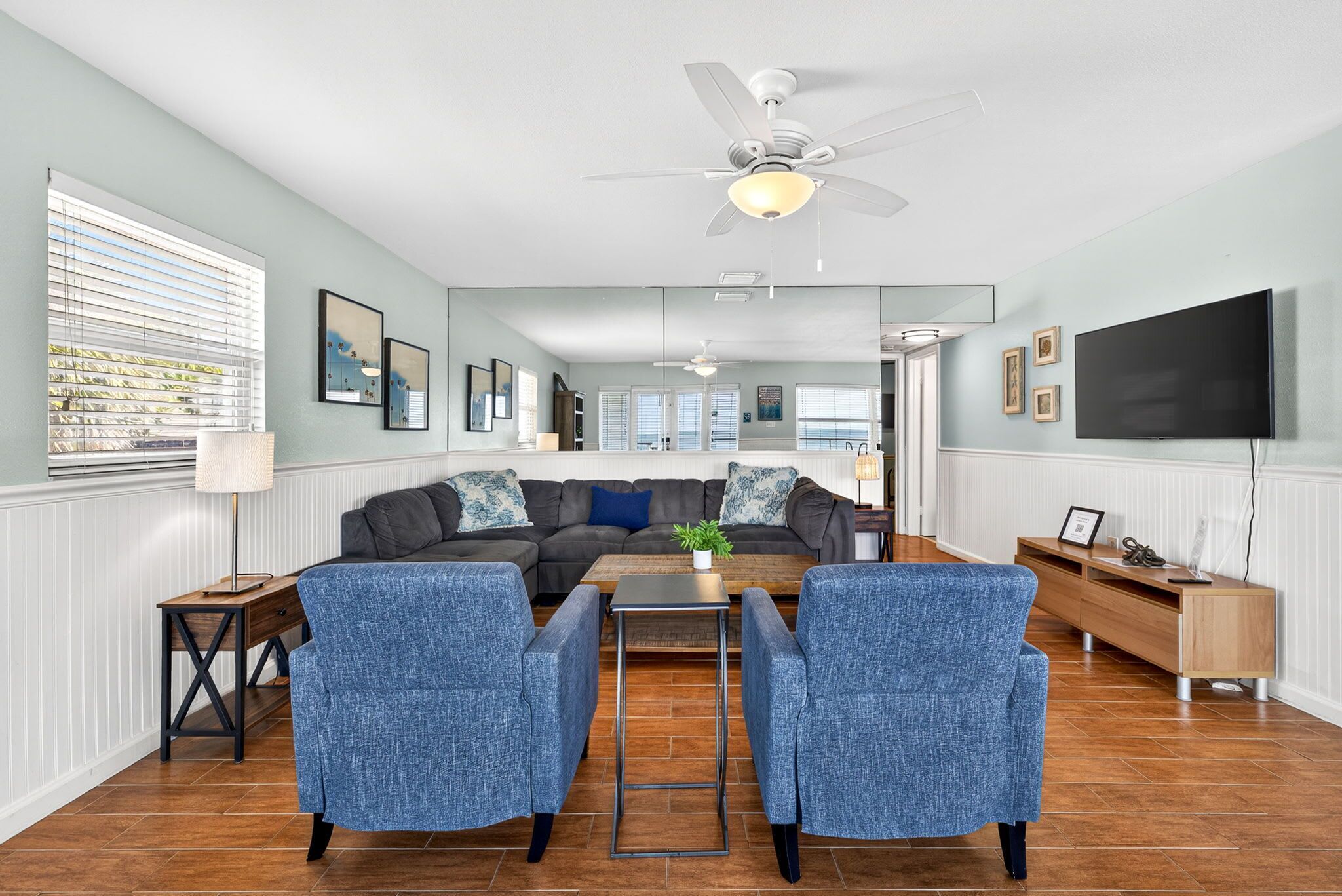 A living room with a sofa, two armchairs, a coffee table, a ceiling fan, and a TV.