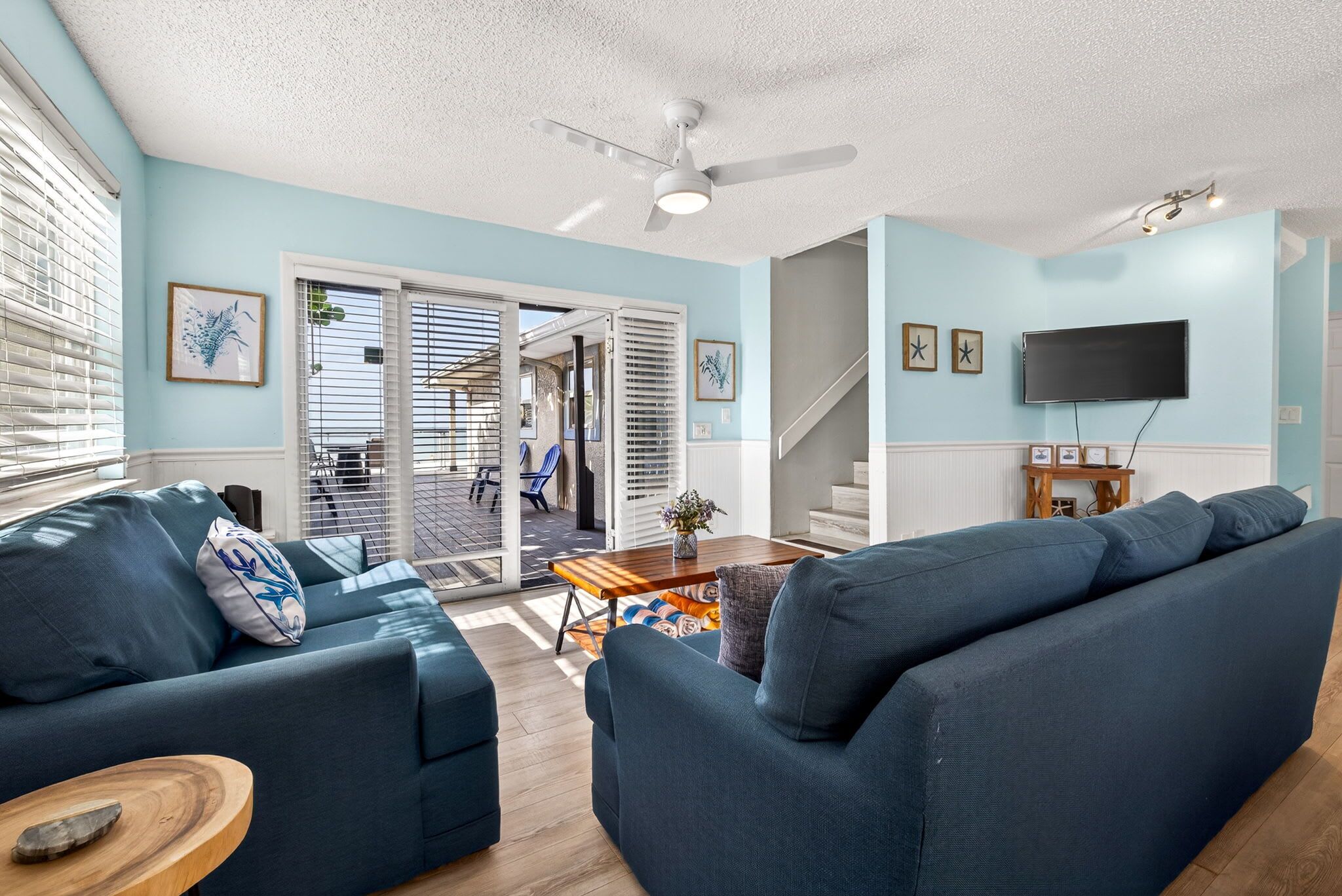 Ein Wohnzimmer mit einem blauen Sofa, einem Holztisch und einem an der Wand befestigten Fernseher.