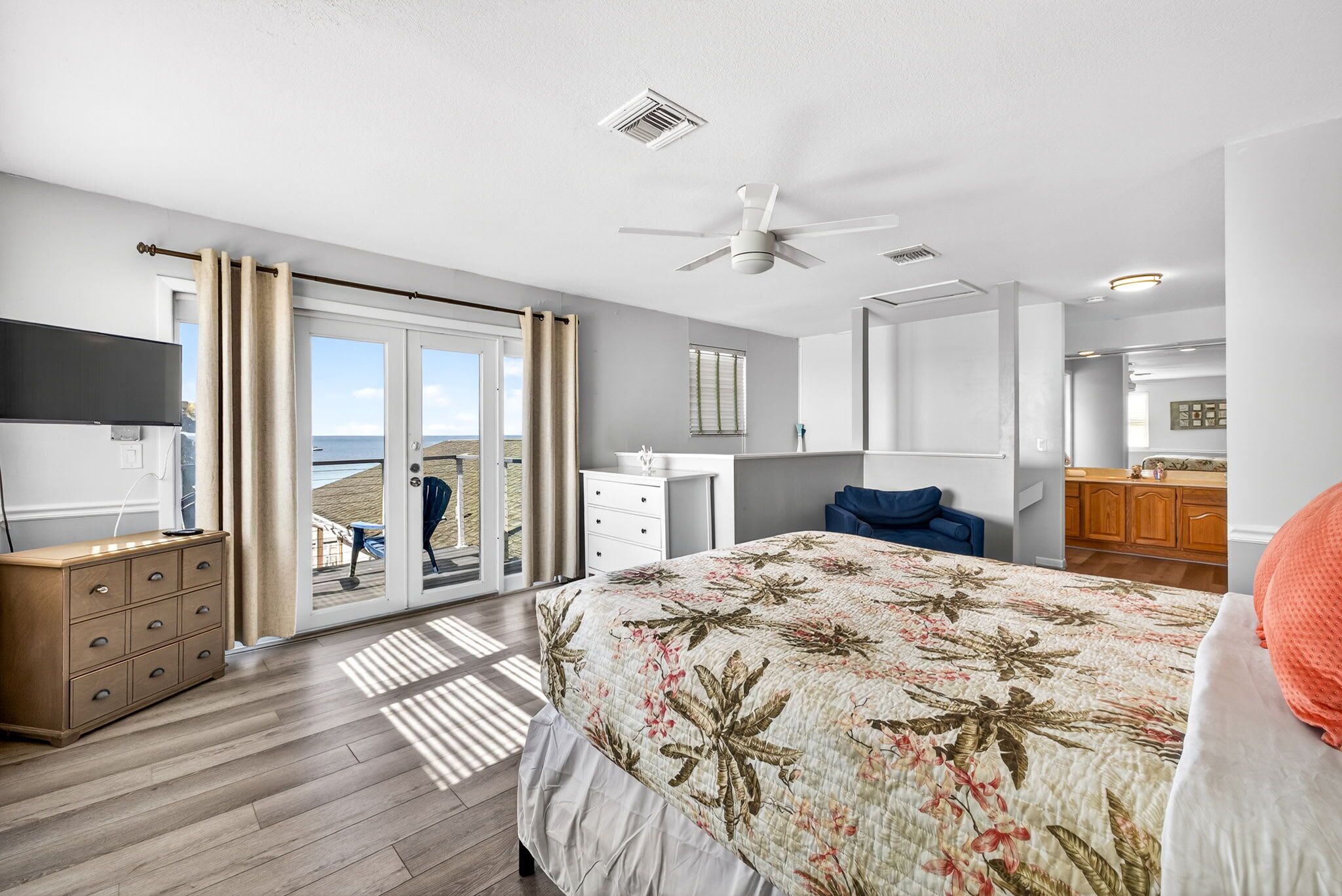 A bedroom with a bed, a dresser, a TV, a ceiling fan, and a view through a sliding glass door.