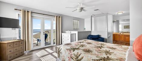 A bedroom with a bed, a dresser, a TV, a ceiling fan, and a view through a sliding glass door.
