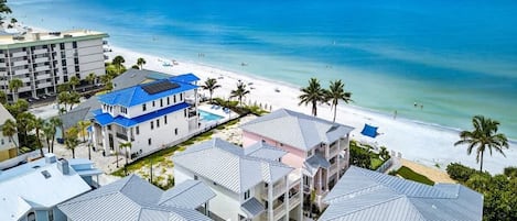 Un hotel frente a la playa con varias edificaciones, una piscina y vista al mar.