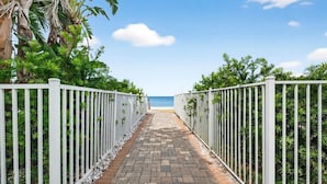 A paved pathway leading to a beach, flanked by white metal fences and lush greenery. - Isla Bonita 4BR Villa in Indian Rocks Beach (Indian Rocks Beach)
