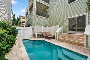 A residential pool area with a clear view of the pool, a white fence, and steps leading to a balcony.