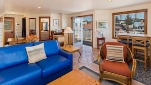 A spacious living area with a blue sofa, a wicker chair, a wooden table, and a balcony with a view of buildings. - San Juan Island, Yakima Suite #1901 (Friday Harbor)