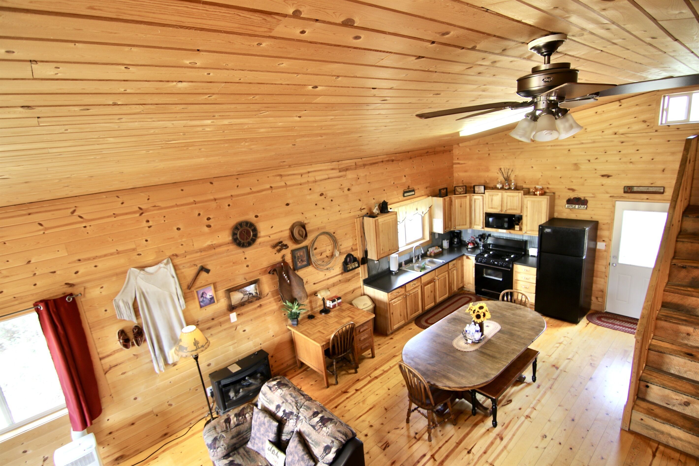 A wooden cabin interior with a dining area, kitchen, and a ceiling fan.