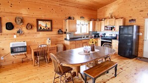 Een houten chalet van binnen met een keukenhoek, eettafel, stoelen en een koelkast.