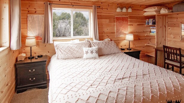 A wooden cabin bedroom with a bed, nightstands, a desk, and a chair.