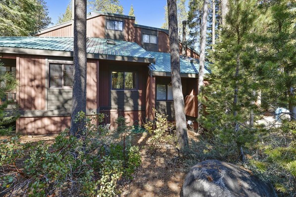 A two-story wooden cabin with a metal roof, surrounded by dense forest and a large rock in the foreground. - The Aspens at Olympic Valley (Squaw Valley)