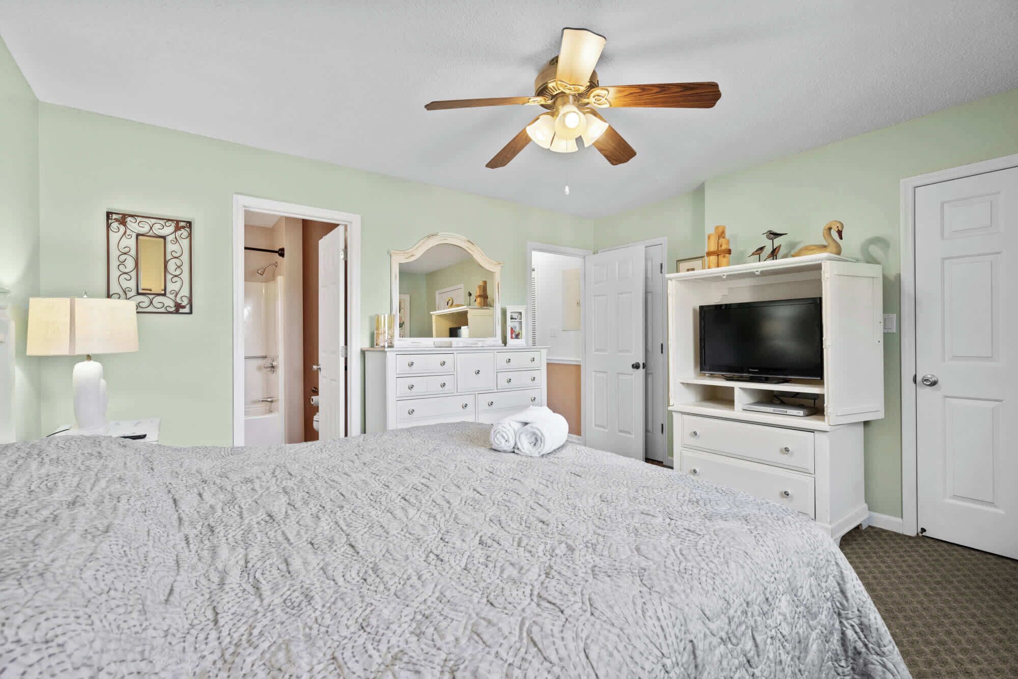 Un dormitorio con cama, ventilador de techo, cómoda, televisor y espejo.