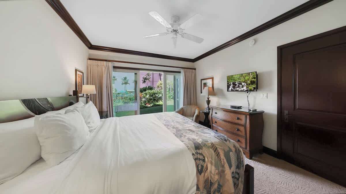 Een hotelkamer met een groot bed, een plafondventilator, een televisie, een dressoir en een deur.