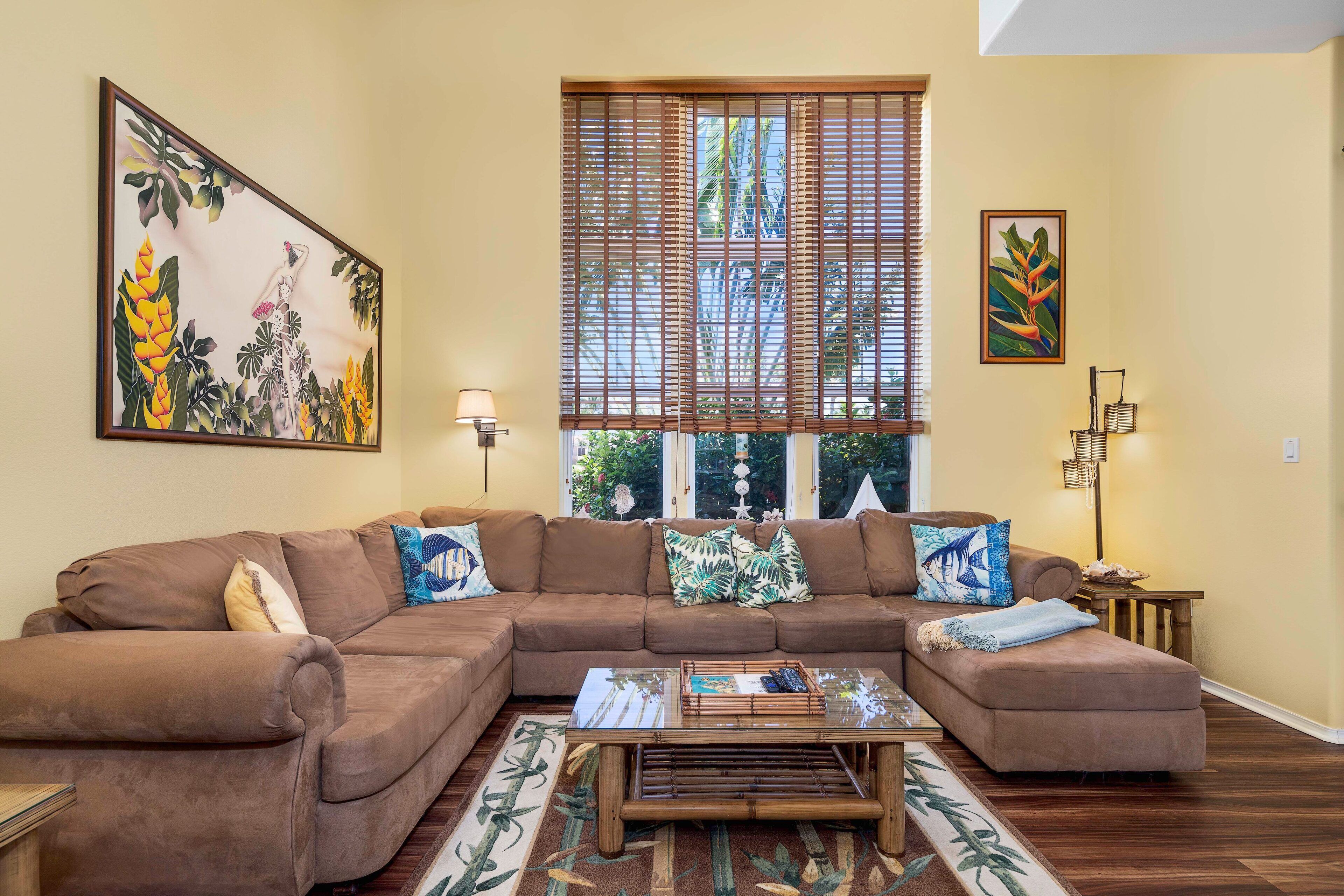 A living room with a brown sectional sofa, a glass coffee table, and a large window with blinds.