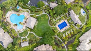 Vista aérea de um resort com piscina, quadra de tênis e jardins ajardinados.