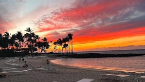 Uma praia com cadeiras de praia e palmeiras sob um céu ao pôr do sol.