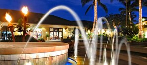 Un hotel amb una font, palmeres i una entrada ben il·luminada.