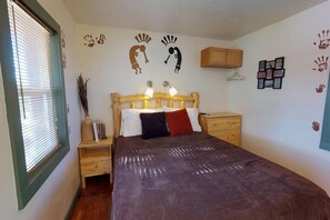 A bedroom with a wooden bed, bedside tables, a window with blinds, and wall decorations including handprints and a picture frame. - Hot Tub, Kokopelli Kabyn, Cute and Cozy! (Blanding)
