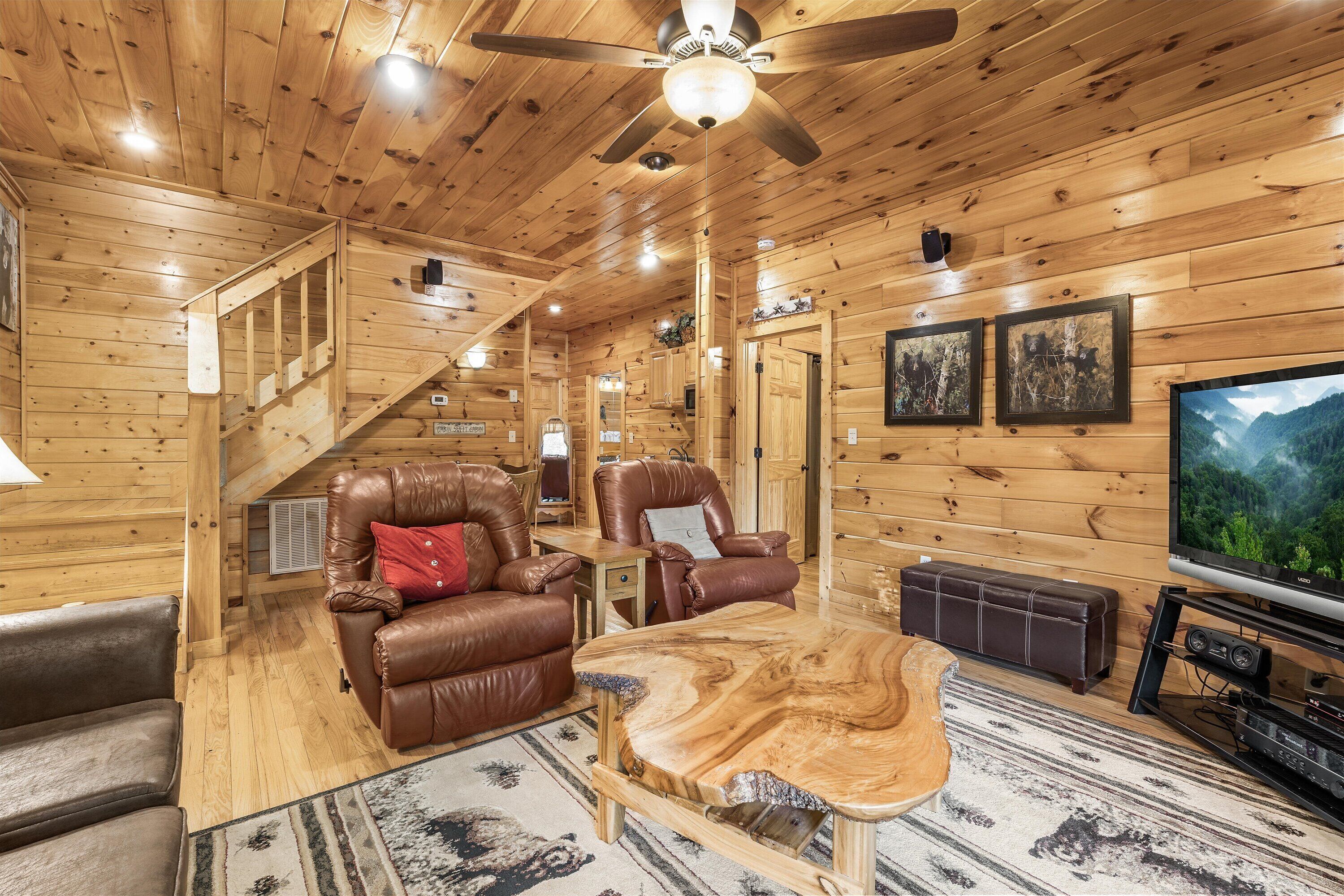 A log cabin interior with a wooden ceiling, leather recliners, a wooden coffee table, a television, and framed pictures on the wall.