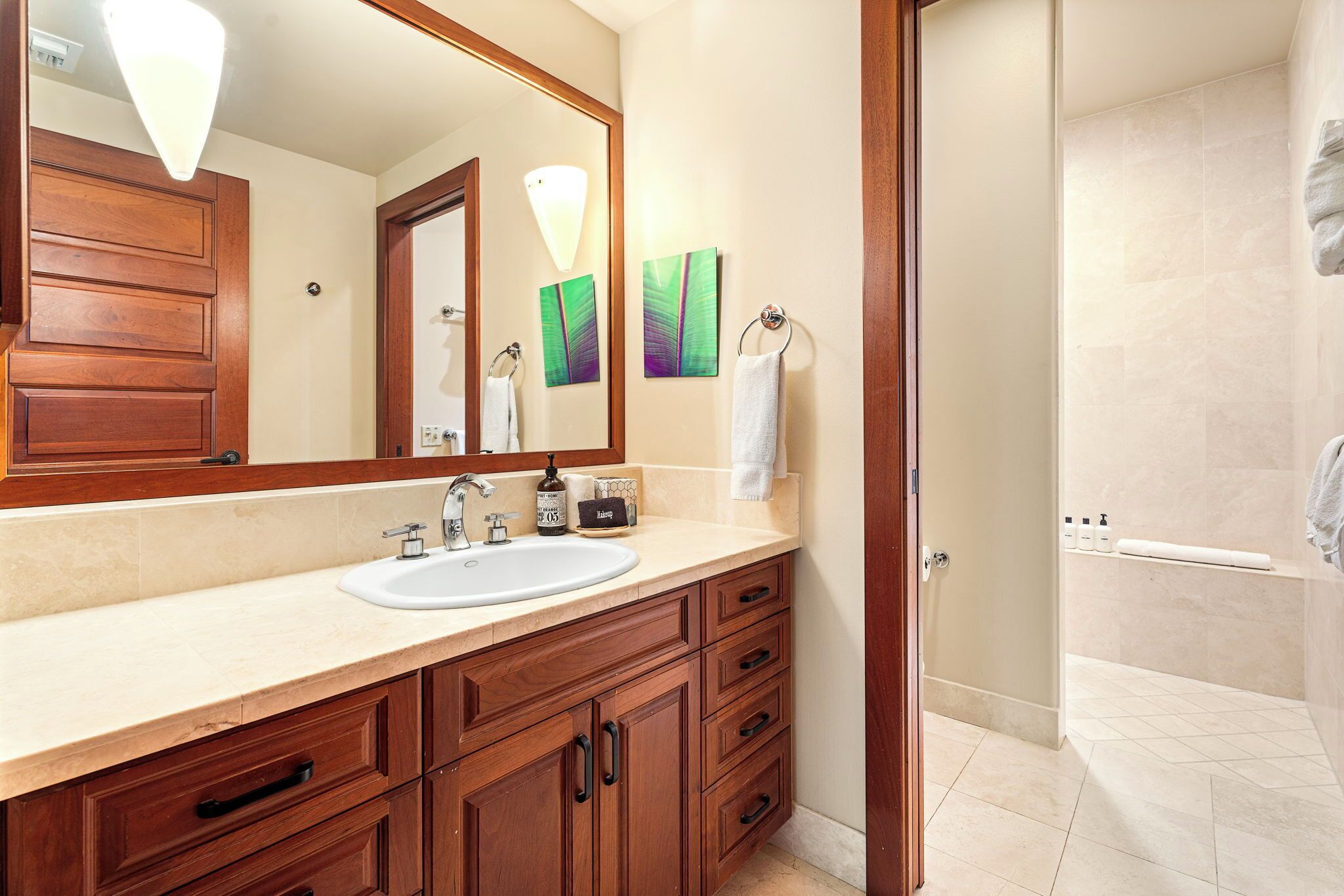 A bathroom with a wooden vanity, a large mirror, a sink, and a shower area.