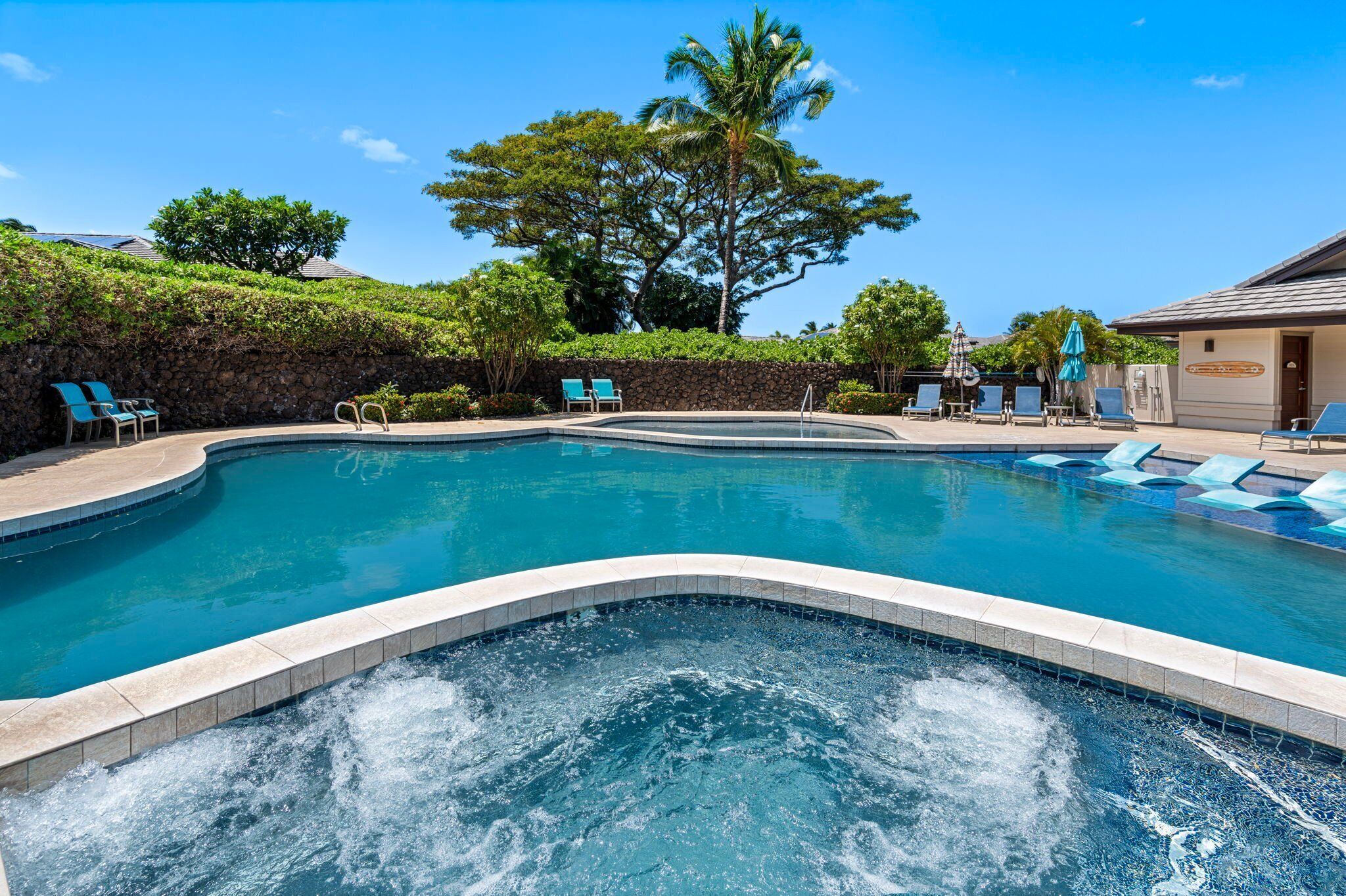 Piscina con sillas de descanso y jacuzzi, rodeada de vegetación y un muro de piedra.