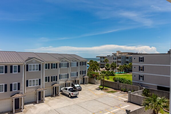 A multi-story residential building with a parking area, a swimming pool, and a view of the ocean.