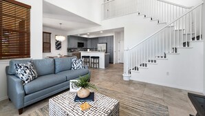 Un salon moderne avec un canapé gris, une table basse agrémentée d’une plante et un escalier menant à l’étage supérieur.