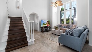 Un salon moderne avec un escalier, un téléviseur, un canapé et une grande fenêtre donnant sur un paysage verdoyant.
