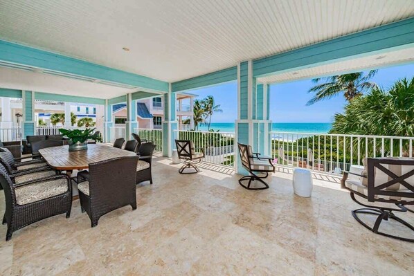 A covered outdoor area with a dining table and chairs, a view of the ocean, and a balcony with a railing.