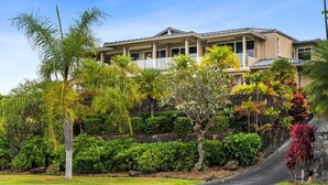 A two-story house with a balcony, surrounded by lush tropical vegetation.