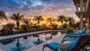 A poolside area with lounge chairs, palm trees, and a sunset view.