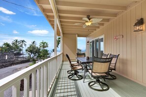 Eine überdachte Veranda mit Tisch und Stühlen, einem Deckenventilator und Blick auf das Meer.