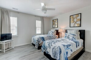 Een slaapkamer met twee bedden, een plafondventilator en kunstwerken aan de wanden.