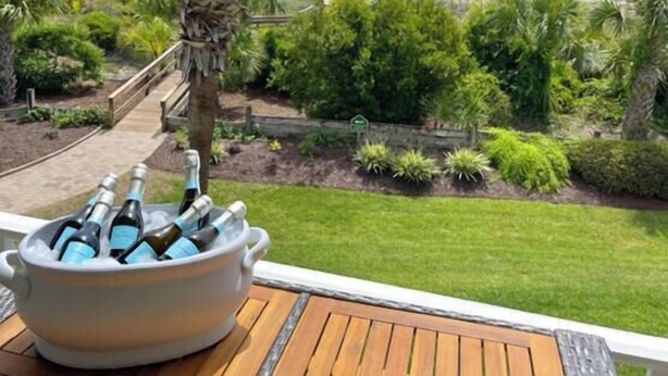 En vy över Beachside Colony, Tybees enda hotellkomplex direkt vid havet, med en träveranda och ett fat fullt av champagneflaskor.