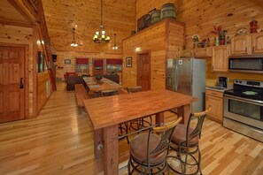 A wooden cabin interior with a dining area, kitchen, and seating.