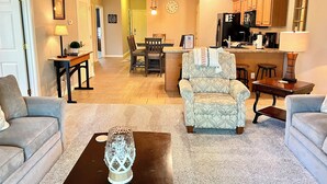 Ein Wohnzimmer mit Couchtisch, zwei Sofas, einer Essecke mit Tisch und Stühlen, einer Küche mit Holzschränken und einer Wanduhr.